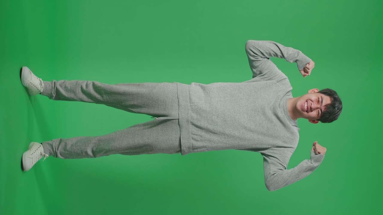 Full Body Of Smiling Asian Man Flex Muscle While Standing In Front Of Green Screen Background