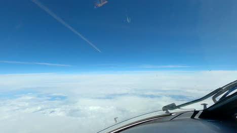 Aircraft-window-POV-flying-across-blue-sky-following-contrail-vapour-trails