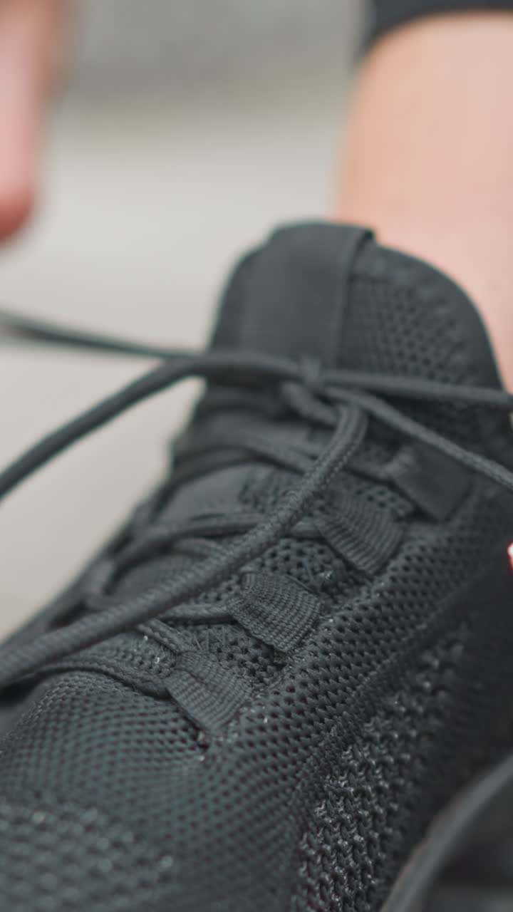 primo piano di una ragazza con una scarpa sportiva nera che si allaccia la scarpa all'aperto, con l'attenzione sulle mani che regolano il laccio, preparandosi per una sessione di esercizi o un allenamento in un ambiente naturale