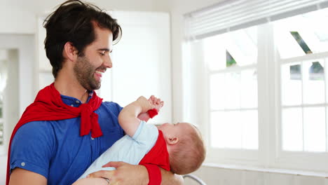 Padre-Feliz-Usando-Una-Capa-Y-Sosteniendo-A-Su-Bebé-También-Con-Una-Capa