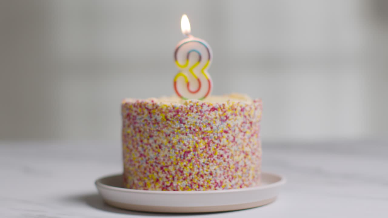 foto de estudio pastel de cumpleaños cubierto con decoraciones y velas encendidas celebrando el tercer cumpleaños que se apaga