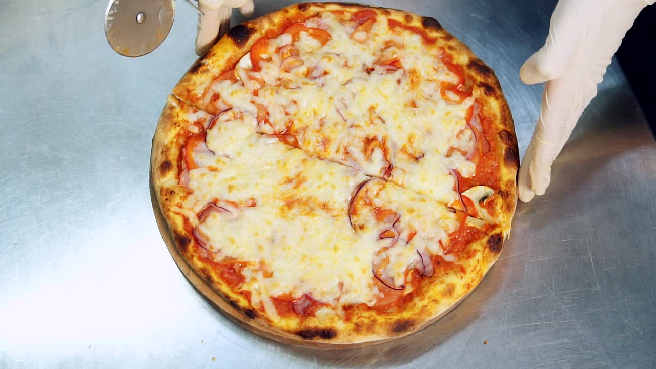 Cutting pizza into pieces with round knife on metal table. Hands of male chef with sharp knife. Hot pizza in the kitchen