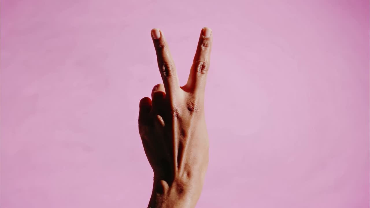 Il video riprende una mano che fa il segno di vittoria su uno sfondo rosa, trasmettendo semplicità.