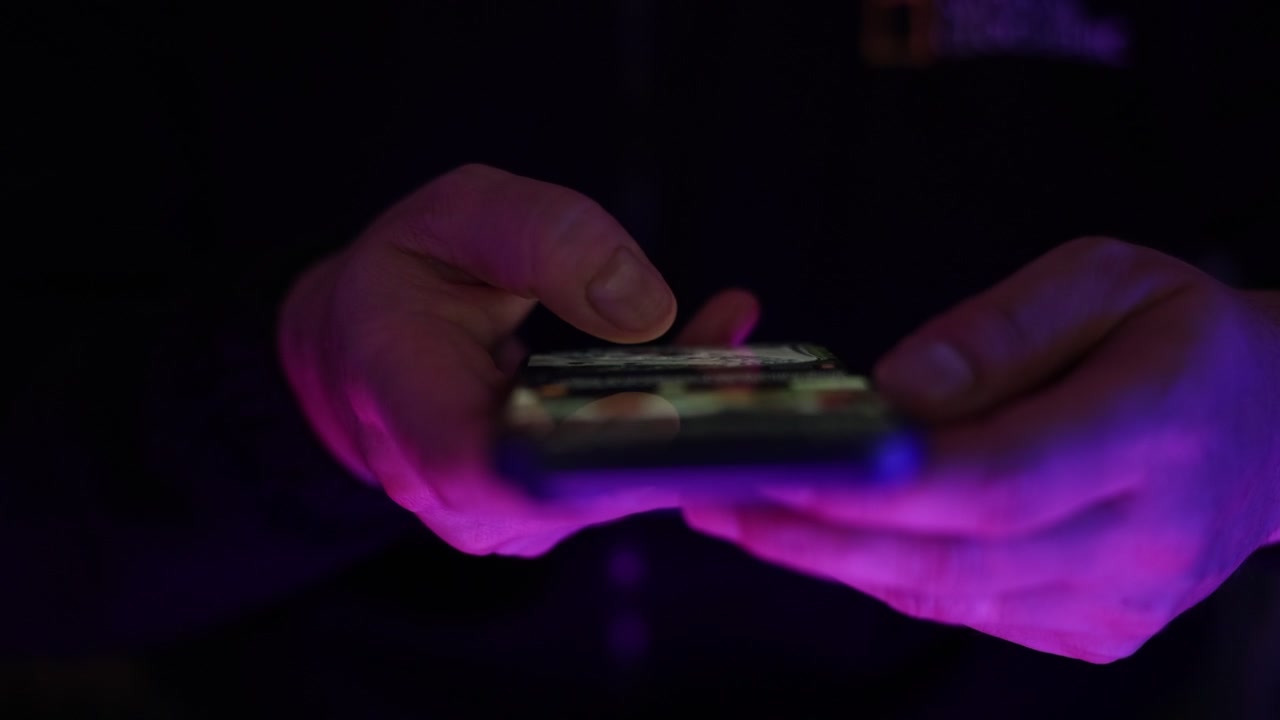 Filmato ravvicinato di una persona che tiene uno smartphone e scorre i contenuti su un dispositivo mobile con lo schermo riflettente