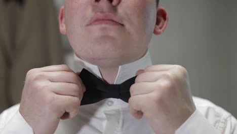 groom adjusts bow tie. preparing to go to the bride. businessman in white shirt. wedding day