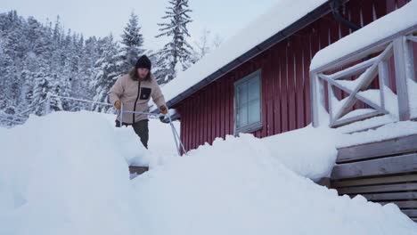 man cleaning scraping snow off the cabin using sleigh shovel in indre fosen, norway - low angle