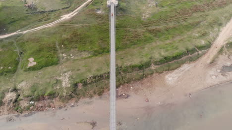 bird's eye view of people crossing suspension bridge over a polluted river