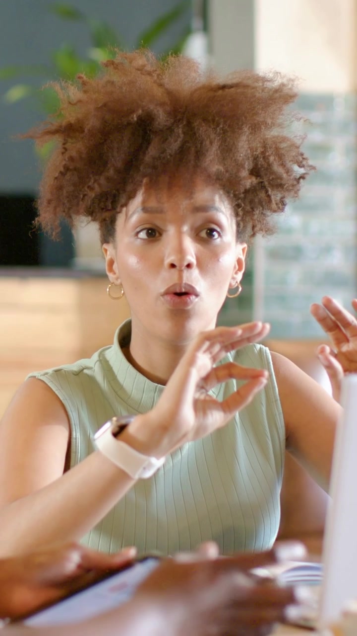 Vertical video: Leaning woman explaining plans after tablet tap at cafe in mint top smartwatch