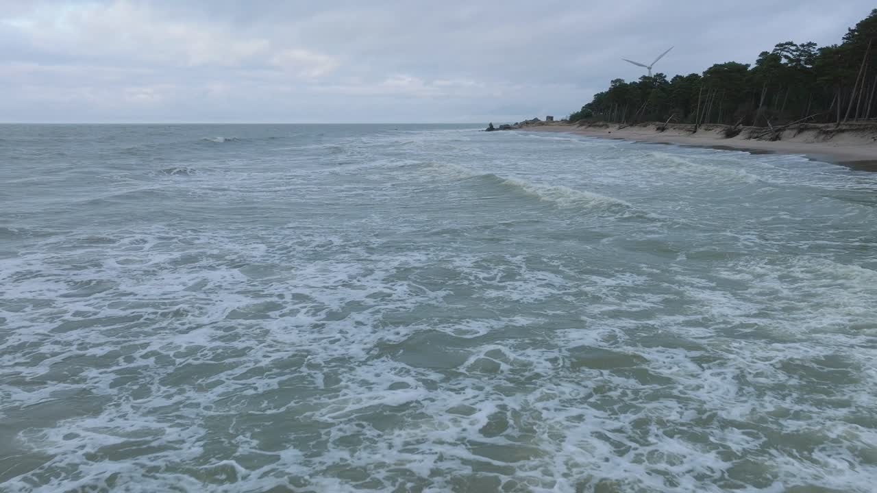 vista aérea de las grandes olas tormentosas rompiendo contra la playa de arena blanca, día nublado, dunas costeras dañadas por las olas, erosión costera, cambios climáticos, amplio tiro bajo de drones avanzando