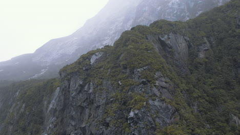 jagged cliuff faces surrounded my mist and fog in the fjords of milford sound in new zealand