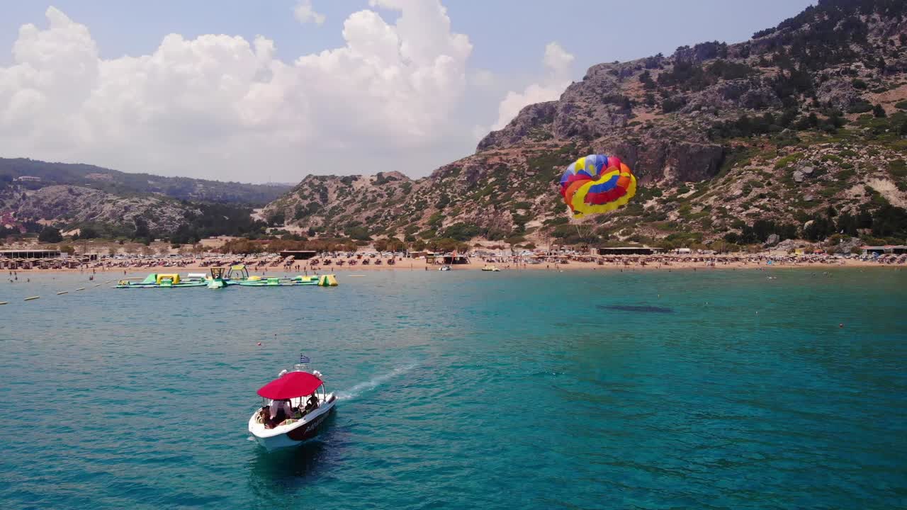 Rodos, Yunanistan'daki Tsambika Plajı'nda renkli paraşütle bağlı turistleri sürat teknesiyle çeken parasailing.