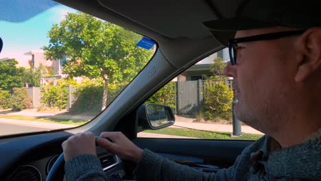 perfil de hombre guapo con gafas y ropa casual conduciendo un coche a través de un suburbio y girando en las rotondas. teniendo una discusión con un tercero y gestando. vista lateral.