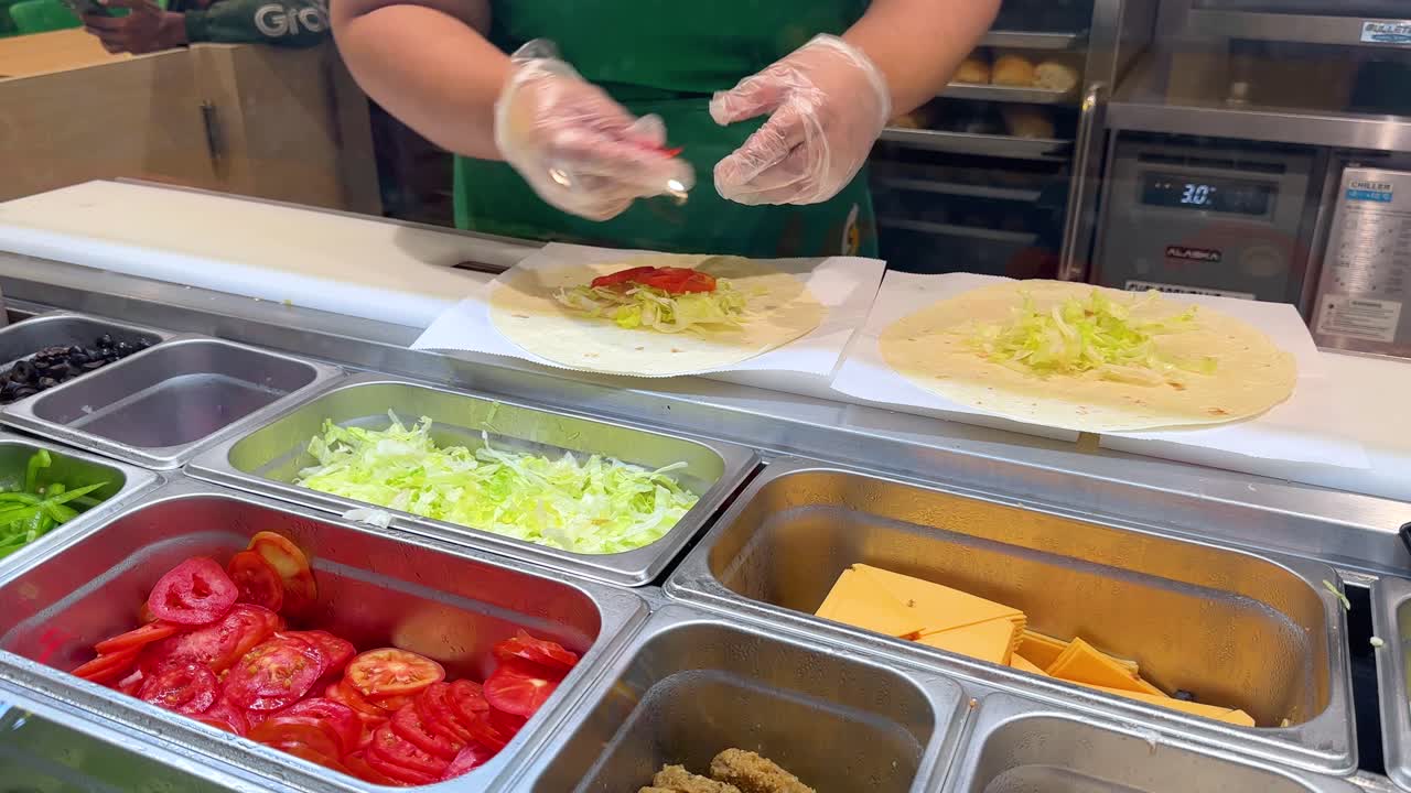 Un addetto alla ristorazione che indossa guanti di plastica assembla fresche tortillas con verdure e formaggio