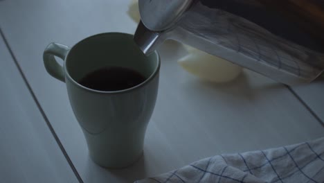 a half-full cup of coffee being filled in through a stainless pitcher