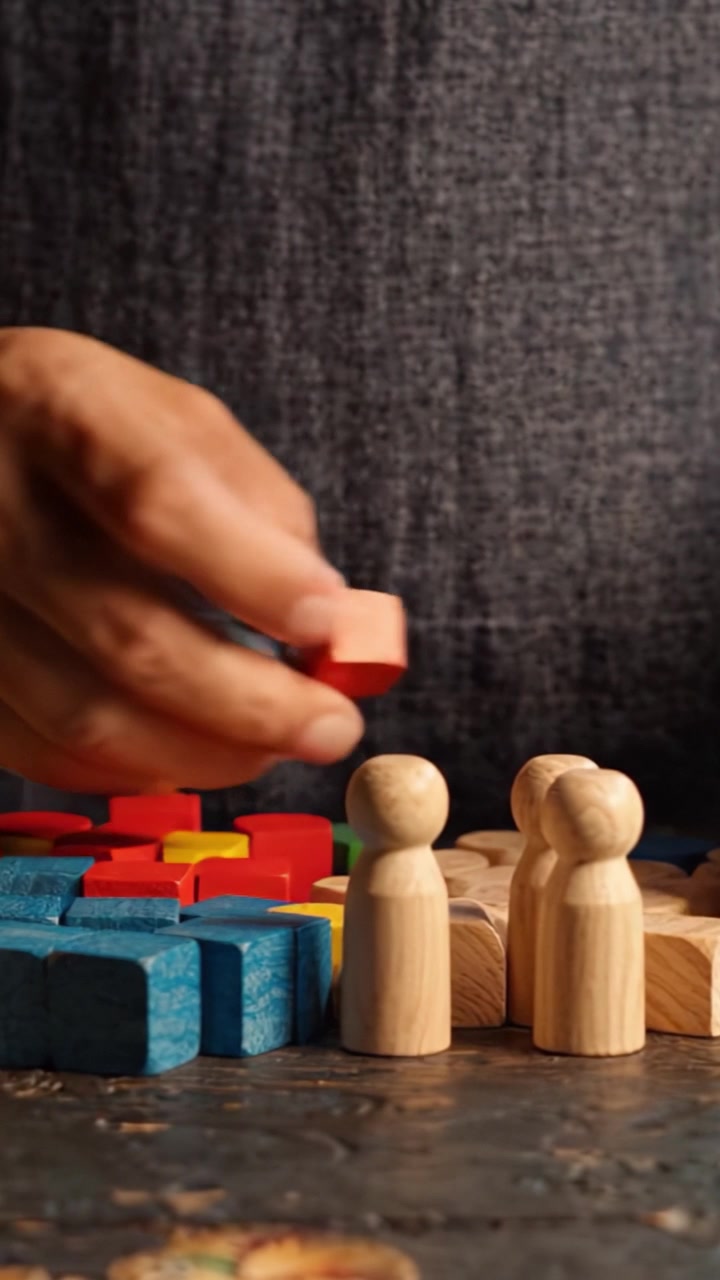 Mãos envolvidas em brincadeiras visuais interativas com blocos de madeira coloridos e figuras em uma superfície texturizada, incentivando a criatividade e a imaginação através da aprendizagem divertida.