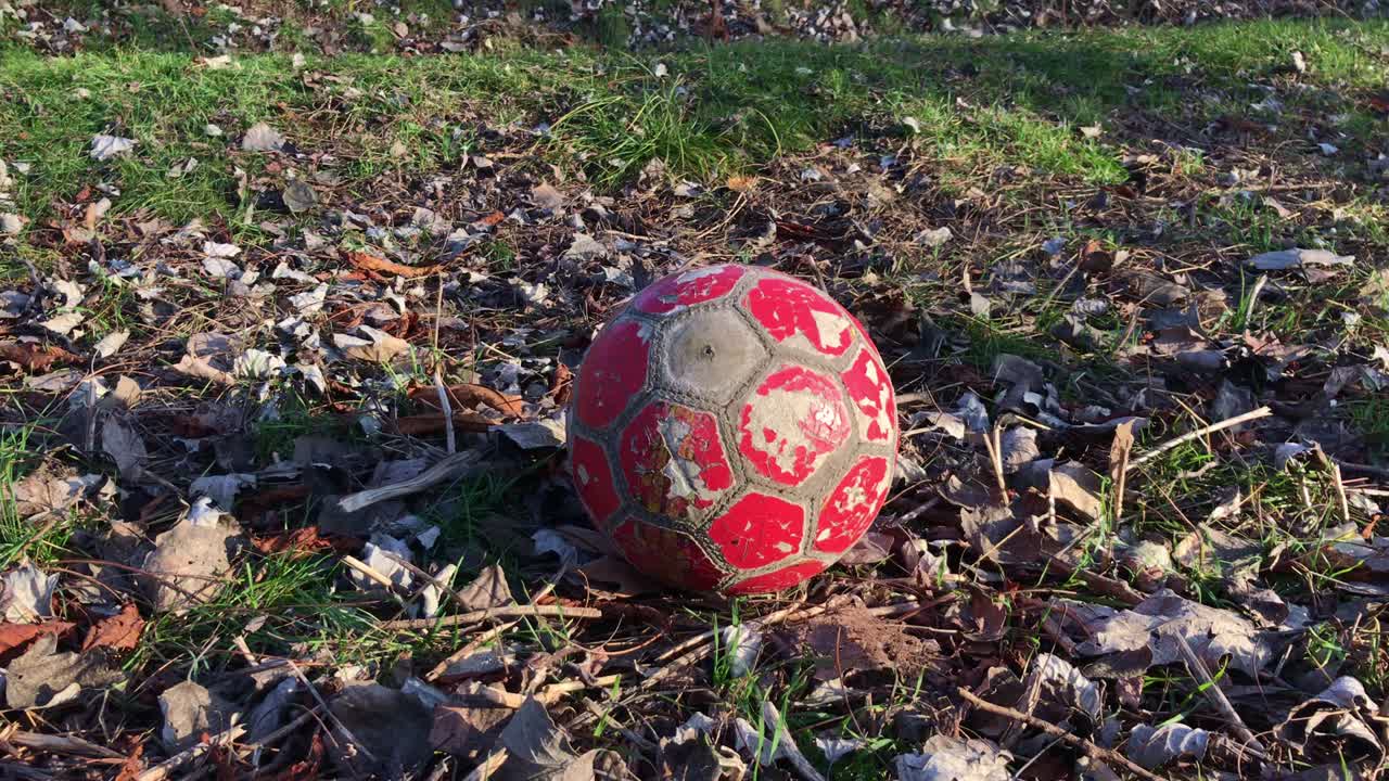 una vieja pelota de fútbol en mal estado yace en el parque en la hierba.