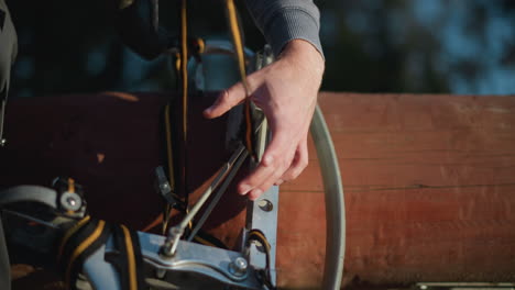 close-up of hands adjusting straps on metallic stilt, wearing gray long-sleeved shirt. background is blurred, emphasizing focus on hands and intricate stilt mechanism