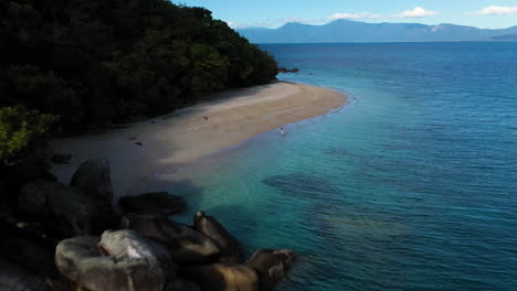 revealing drone shot of woman walking in the water at fitzroy island beach in australia
