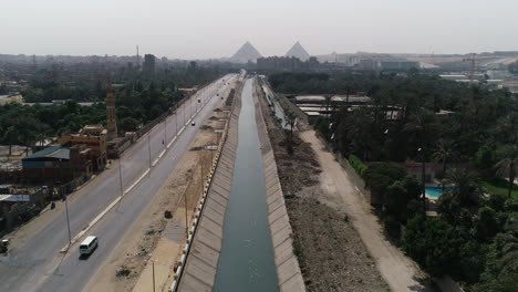 aerial shot track out and rising up for the pyramids of egypt in giza in the background of a branch of the river nile in the foreground maryotya branch and birds are passing in the front