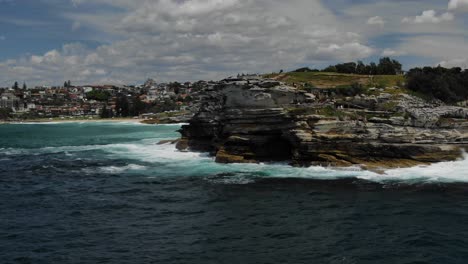 people on rocky promontory of bondi beach with city in background, australia