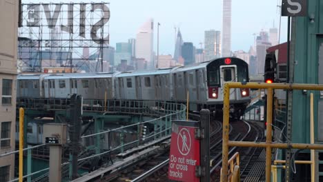 Incoming-Train-at-Queensboro-Plaza-subway-station-with-the-Silvercup-Studios-and-the-Manhattan-skyline-in-the-background,-filmed-in-the-early-morning-hours-of-a-sunny-day-in-New-York-City