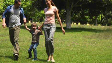 Little-boy-and-parents-running-towards-camera-in-the-park-holding-hands