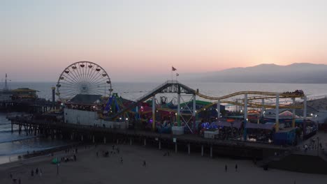 Toma-Aérea-Panorámica-Baja-Del-Muelle-De-Santa-Mónica-En-Una-Bulliciosa-Noche-De-Verano-Al-Atardecer