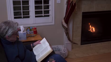 old senior woman reading a book by the fireplace on a lonely christmas night