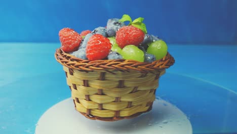 rotating wooden basket with different forest berries close-up on a blue wooden table. 4k slow motion loop video with speed ramp effect.