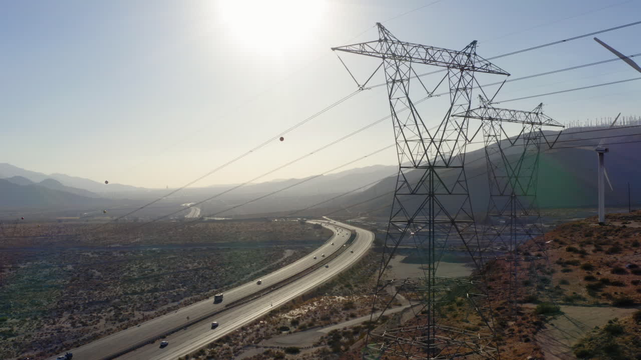 vista aérea panorámica de derecha a izquierda junto a turbinas eólicas y líneas de transmisión de alto voltaje que revelan carreteras y montañas cerca de palm springs en el desierto de mojave, california, ee.uu.