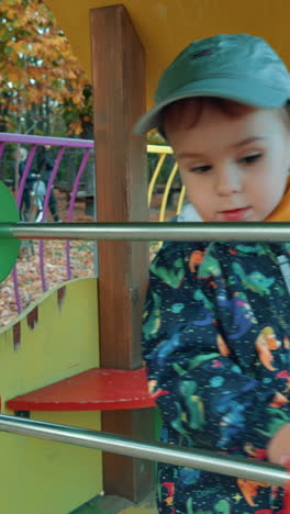 lovely caucasian toddler playing with big abacus on the playground. male kid having good time outdoors in autumn. vertical video