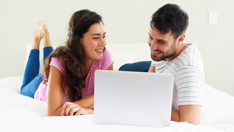 pareja interactuando entre sí mientras usan una computadora portátil en la cama