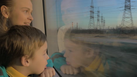 small boy with mother sitting against window in their rail train place and watching outside