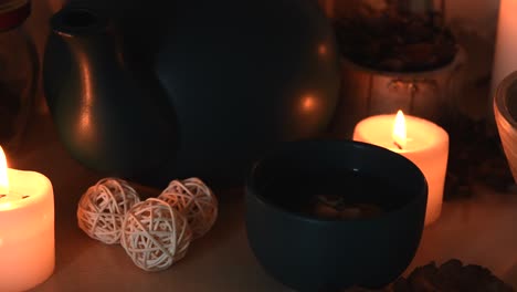 relaxing background detail shot of an herbal tea on a green cup, with steam coming out, near candles with flickering flames, a tea pot and some herbs