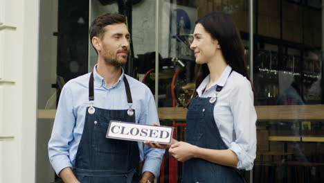 Attractive-Smiled-Woman-And-Man,-Workers-Of-The-Restaurant,-Standing-On-The-Street-At-The-Door-Looking-At-Each-Other-And-Then-To-The-Camera