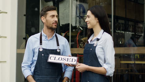 attractive smiled woman and man, workers of the restaurant, standing on the street at the door looking at each other and then to the camera