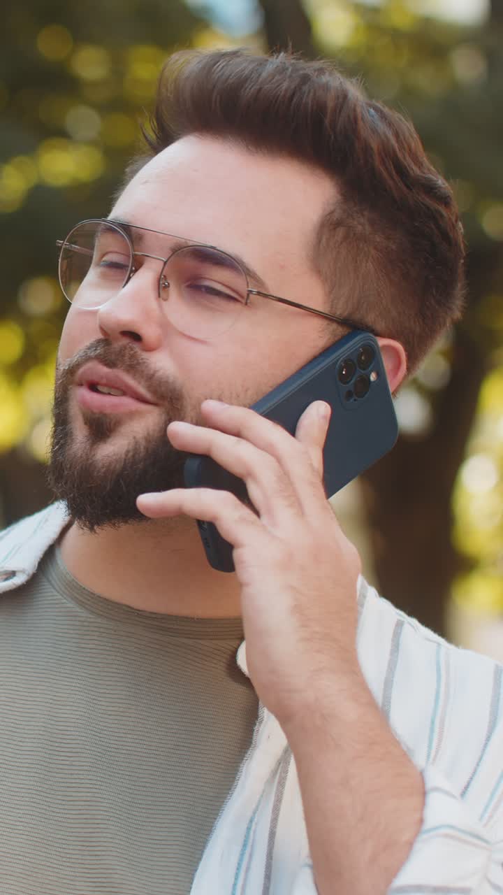 Giovane turista caucasico felice in abiti casual che parla al telefono mentre è in piedi su una strada cittadina.