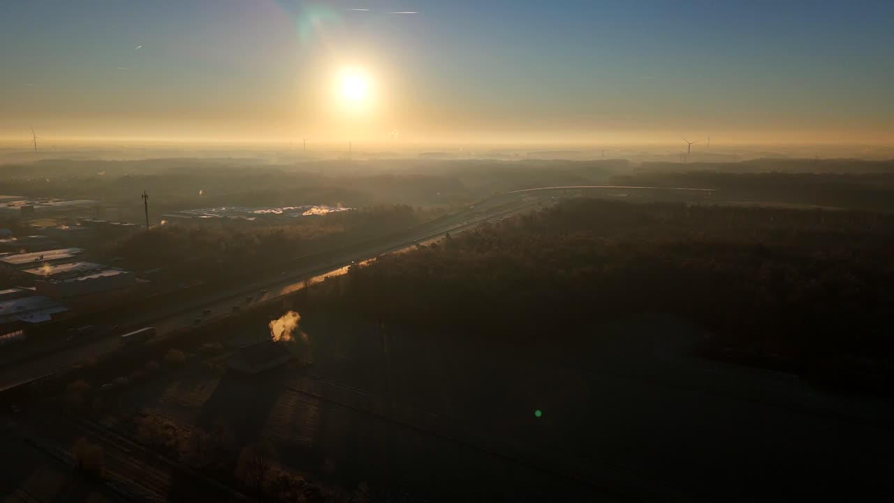 Aerial establishing shot of traffic scene on american highway during foggy sunrise. Wide shot. Golden hour with forest trees and cars on freeway. Industrial area.Tranquil atmosphere during cold winter