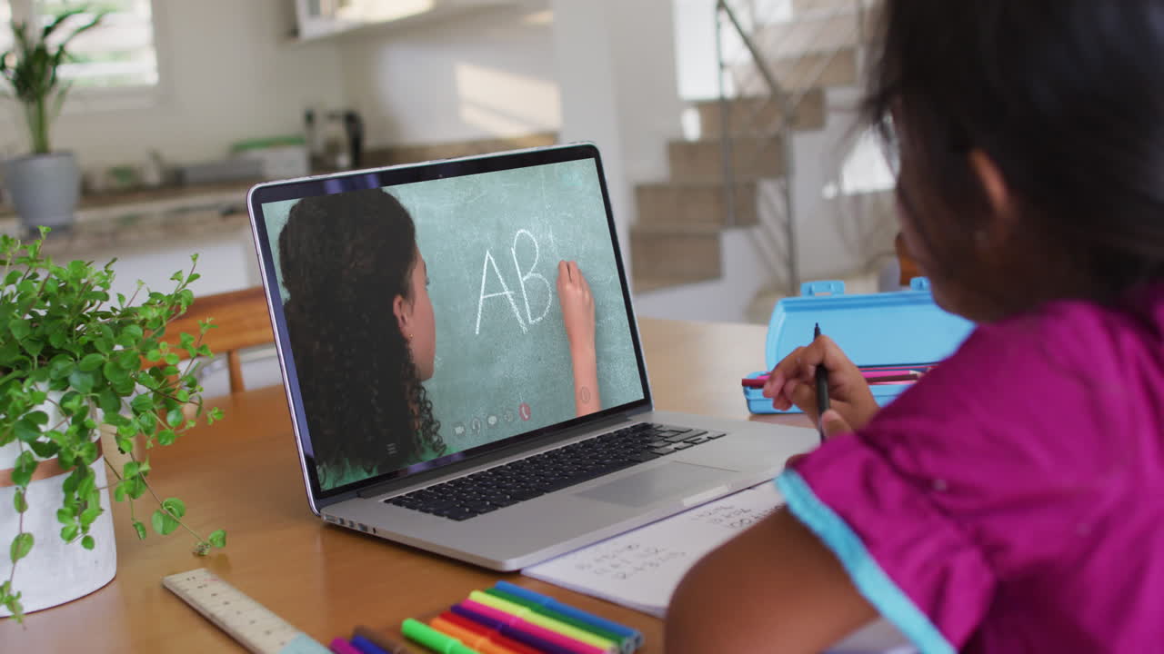 African american girl doing homework while having a video call with female teacher on laptop at home