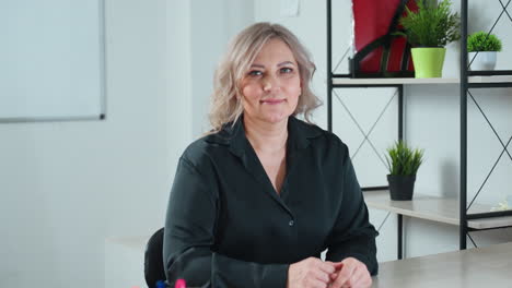 client looking with warm smile seated in well lit office with modern decor and indoor plants arranged neatly on shelf behind desk conveying friendly welcoming atmosphere in business setting