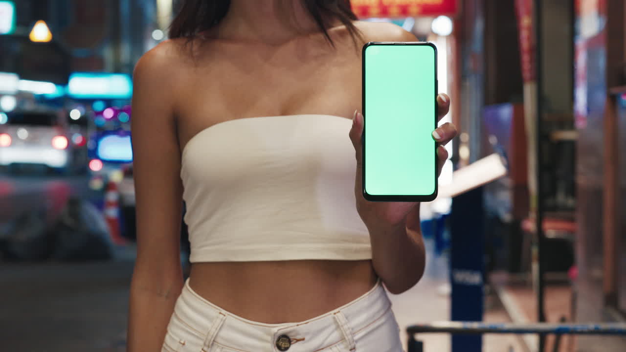 Woman Holding Smartphone with Green Screen on City Street at Night