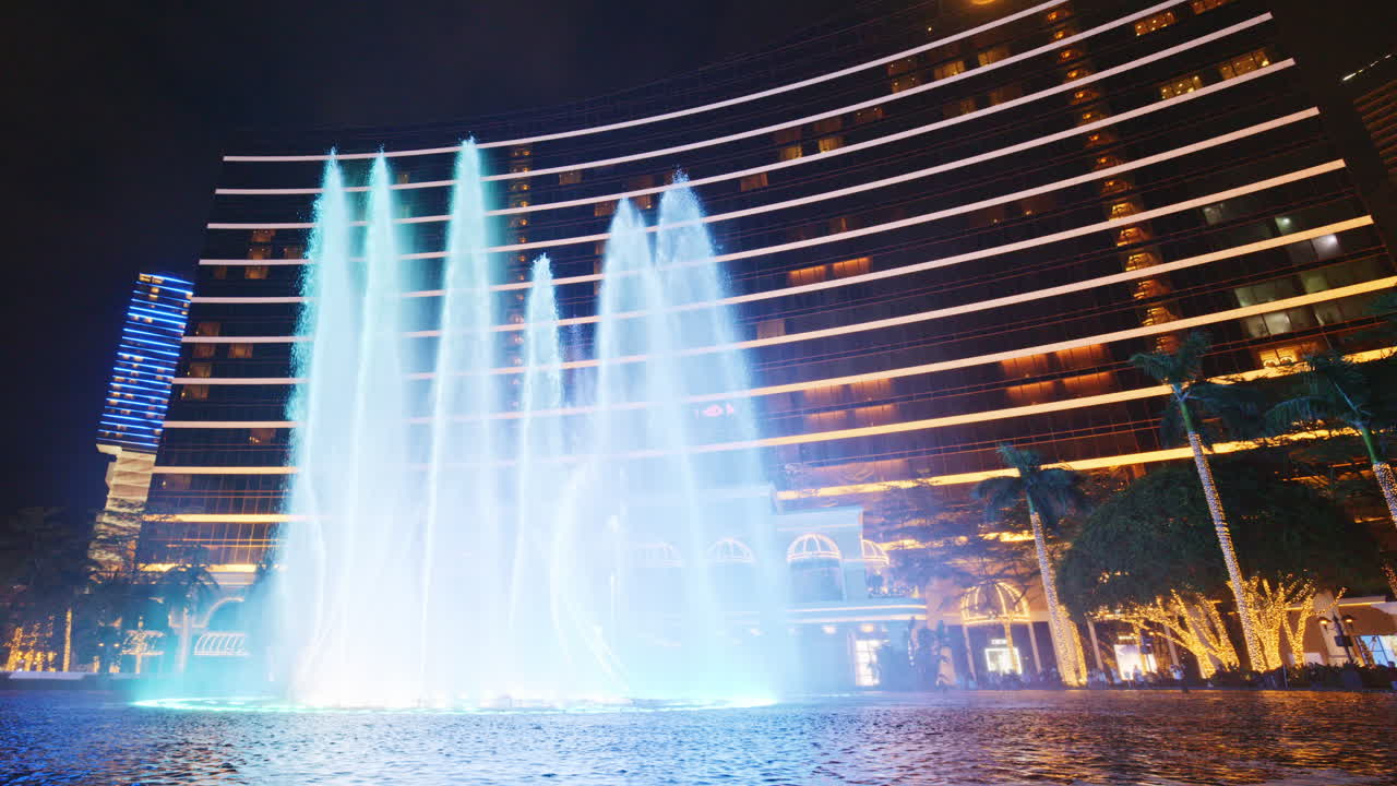 Espectáculo dinámico de fuentes con luces de colores frente a un hotel de lujo