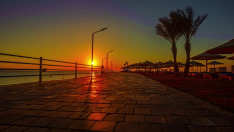 Deserted-seafront-promenade-with-yellow-sun-at-horizon-and-beautiful-colorful-sky-over-sea-at-sunset