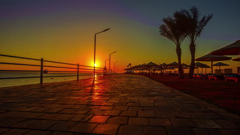 deserted seafront promenade with yellow sun at horizon and beautiful colorful sky over sea at sunset