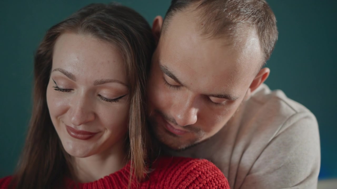 Un primo piano ravvicinato mostra una giovane coppia che si scambia un abbraccio affettuoso, con l'uomo che si china sulla spalla della donna, una leggera inclinazione della testa, espressioni rilassate, un tocco delicato e un'atmosfera calda e romantica, con coppia, abbraccio