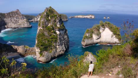 mujer joven caminando hacia el borde del acantilado costero con vistas a las islas rocosas tropicales de nusa penida