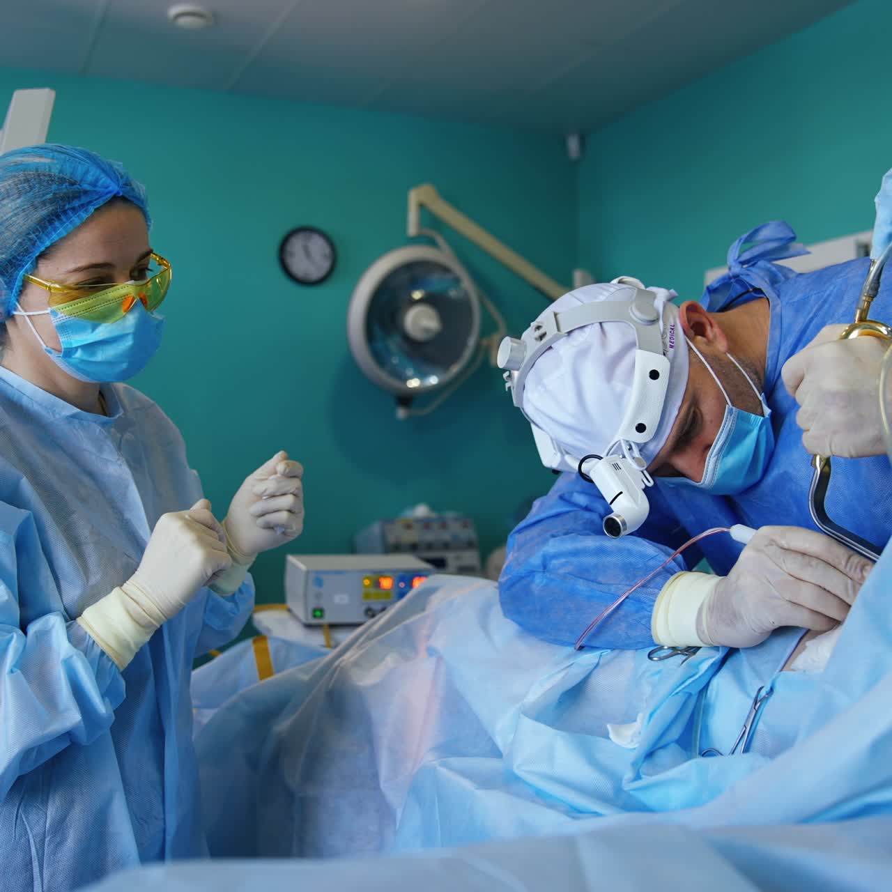 Surgeon performing breast implantation procedure. Doctor uses tool holding the upper skin creating cavity for bust implant. Nurse standing beside