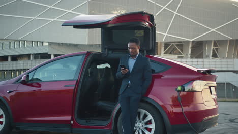 hombre de negocios usando el teléfono al lado de un ev