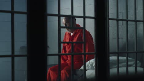 criminal sits on the bed in prison cell looks at barred window          (stock footage)