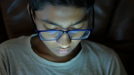 Teenage-boy-sitting-on-sofa-using-smart-phone-at-night